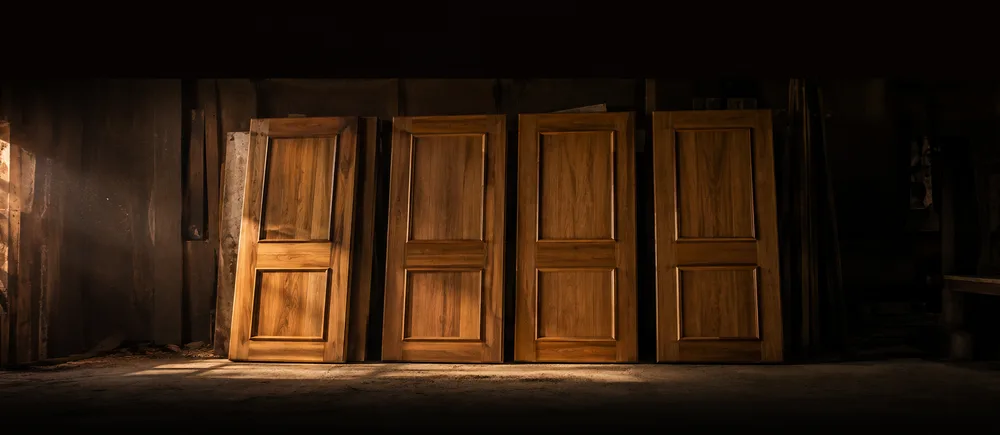 Four finished solid teak doors leaning in a row against the workshop wall